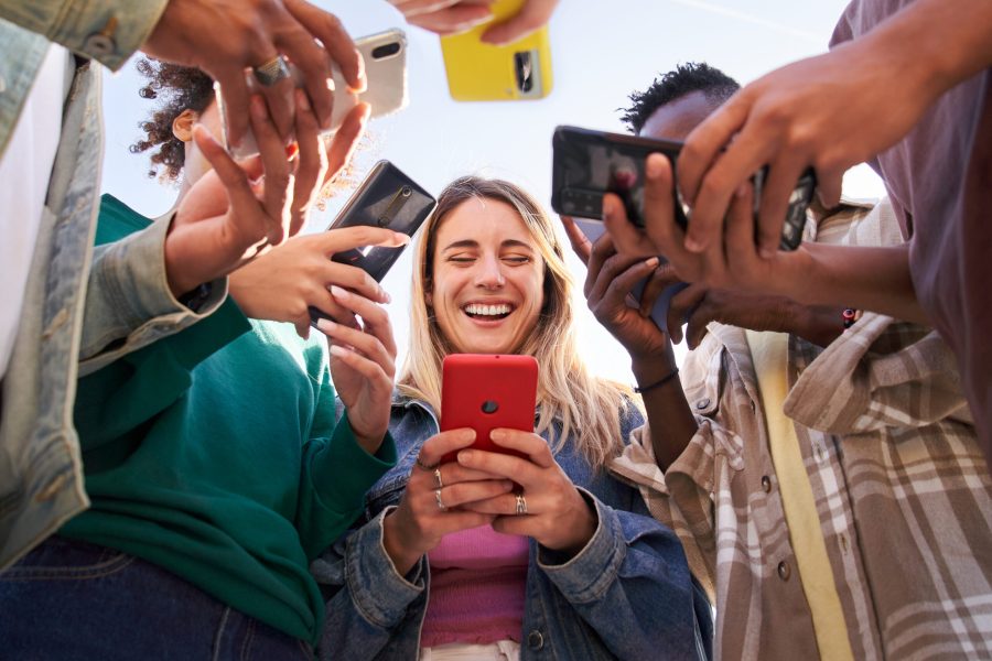 Low angle view of a group of young teenagers friends using cell phones and walking in the city. Concept of community millennial people addicted to technology. Social Media communication generation Z